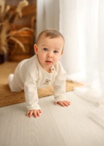 Baby crawling on a wooden floor with natural light in a professional baby photography session.