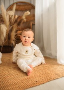 Baby sitting on a woven rug with natural light and boho decor during a baby photography session.