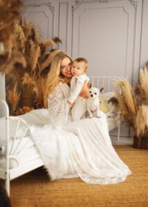 Smiling mother holding her baby with a small dog in a boho-style baby photography session.
