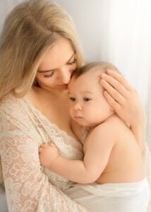 Mother gently cuddling her baby during a baby photography session with soft natural light.