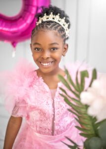 Adorable birthday photography of a little girl in a pink dress and crown, celebrating with a balloon.