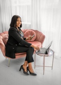 Smiling woman in a black suit using her phone and laptop during a business photography session.