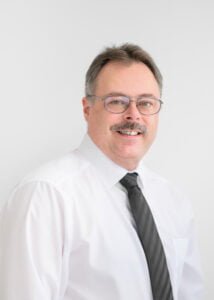Business photography headshot of a professional businessman in a white shirt and glasses.