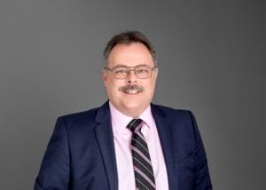 Business photography headshot of a middle-aged businessman in a suit and tie with a confident smile.