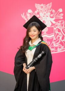 Female graduate holding diploma in cap and gown in front of Nottingham University crest