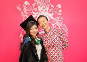 Female graduate with her friend in front of Nottingham University crest