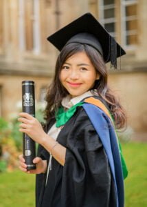 Female graduate holding diploma in cap and gown at Nottingham University campus