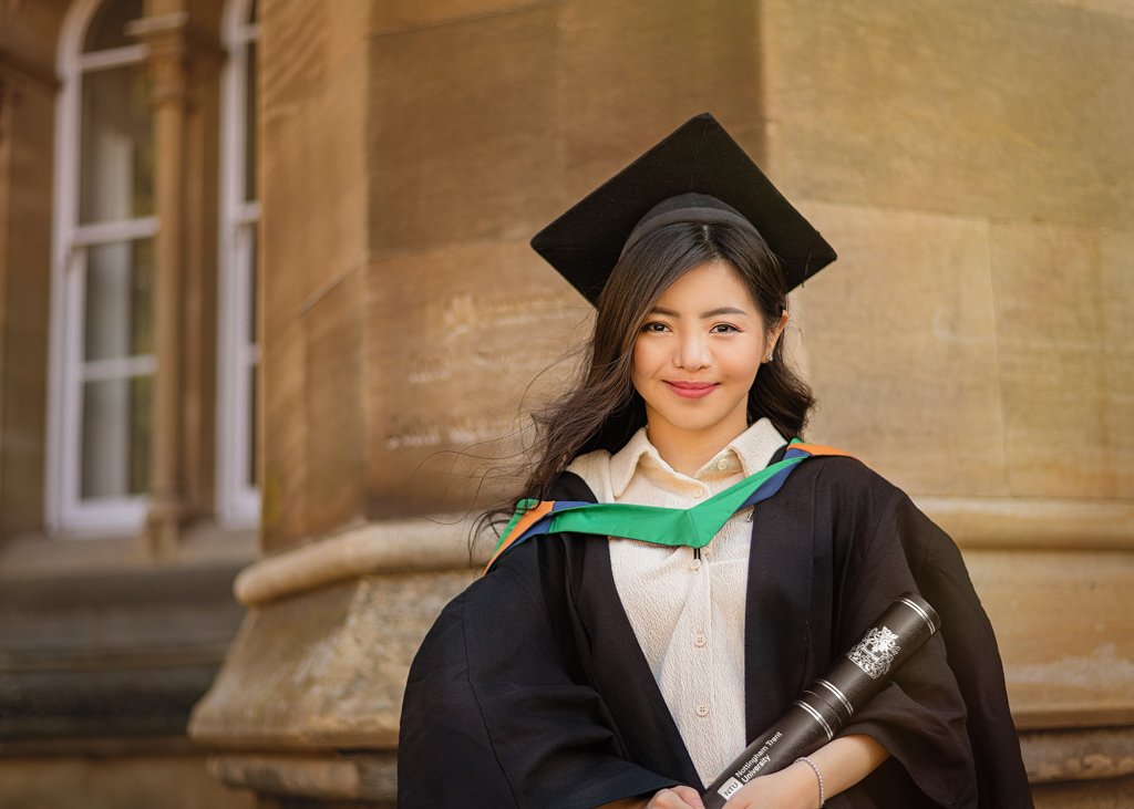 Female graduate holding diploma in front of historic building at Nottingham University