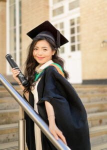 University of Nottingham graduate smiling with diploma on campus stairs, capturing the spirit of graduation day