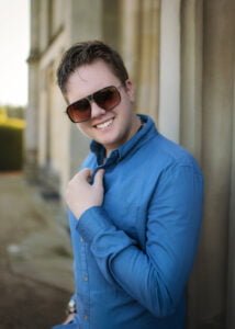 Outdoor men’s photoshoot with a confident man in a blue shirt and sunglasses, radiating charm.