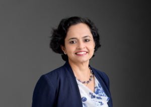 Business photography headshot of a smiling businesswoman in a navy blazer against a dark gray background.