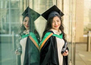 University of Nottingham graduate smiling with her diploma, reflection in glass showcasing her pride and joy.
