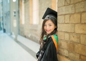 Female graduate in cap and gown leaning against wall at Nottingham University