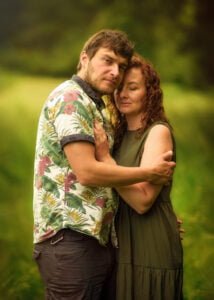 A tender moment between a couple, nestled in nature, with the man embracing the woman from behind