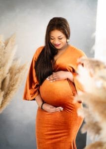 Glowing expectant mother in a burnt orange maternity gown holding her bump during an intimate maternity session.