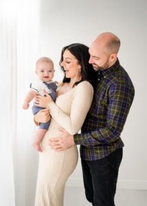 A joyful family moment in a Nottingham studio, with parents lovingly gazing at their baby, enveloped in a warm embrace.