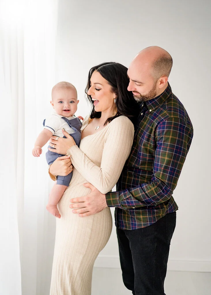 A joyful family moment in a Nottingham studio, with parents lovingly gazing at their baby, enveloped in a warm embrace.