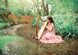 Business photography portrait of a musician playing the harp in an outdoor natural setting.
