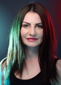 Portrait of a woman with striking dual-toned hair and a contemplative gaze, highlighted by colored studio lighting.
