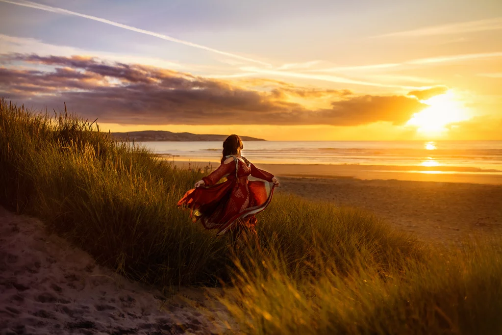 Woman in red dress enjoying a seaside sunset in a professional portrait.