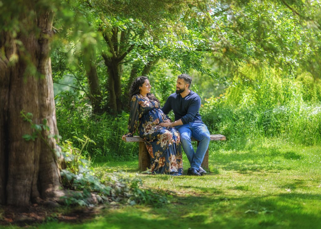 A couple sits serenely on a bench in a lush garden, surrounded by the tranquility of nature, sharing a moment of tender anticipation.