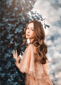 Woman wearing champagne glitter dress standing near ivy-covered wall