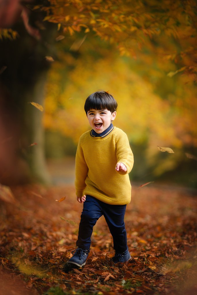 Autumn portrait if a boy with leaves in Wollaton Hall Park in Nottingham with family photographer