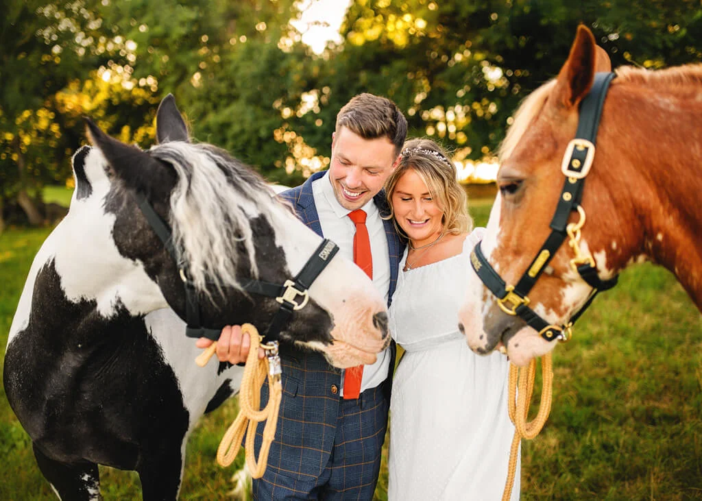 Joyful newlyweds laughing with horses in a pastoral Nottingham setting, embodying rustic couple photography.