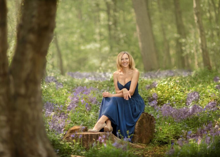 Woman in a blue dress sitting on a tree trunk in bluebell wood in Nottingham during family and kids photoshoot