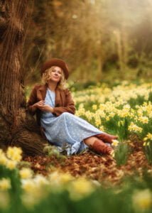 A woman in a vintage outfit sits among a sea of blooming daffodils in a Nottingham spring, contemplating the beauty around her.
