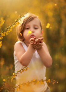 Child blowing yellow flower petals in a sunlit field, captured by Eastwood's family photographer in Nottingham.