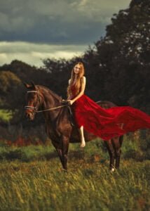 Woman in a red dress riding a horse in a field during an elegant equine photoshoot