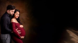 Expectant couple embracing during a heartfelt maternity session, with the mother-to-be in a red gown and her partner in a black shirt.