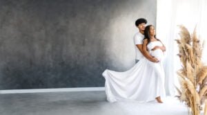 Expectant parents share a tender moment during their maternity session in a light-filled studio with pampas grass.