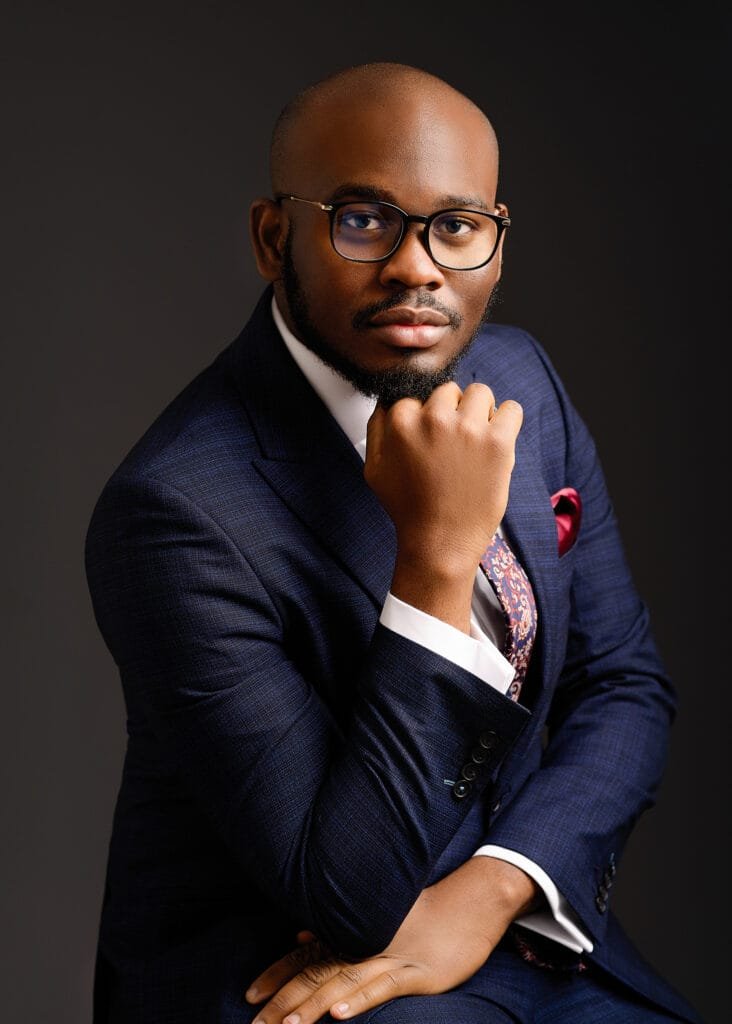 Business photography headshot of a professional man in a navy suit and glasses, posing confidently.