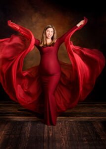 Expectant mother in a flowing burgundy gown radiates joy in a creative maternity photography session.
