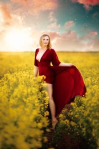 Elegant woman in a red dress standing amidst a vibrant yellow rapeseed field under a dreamy Nottingham sky.