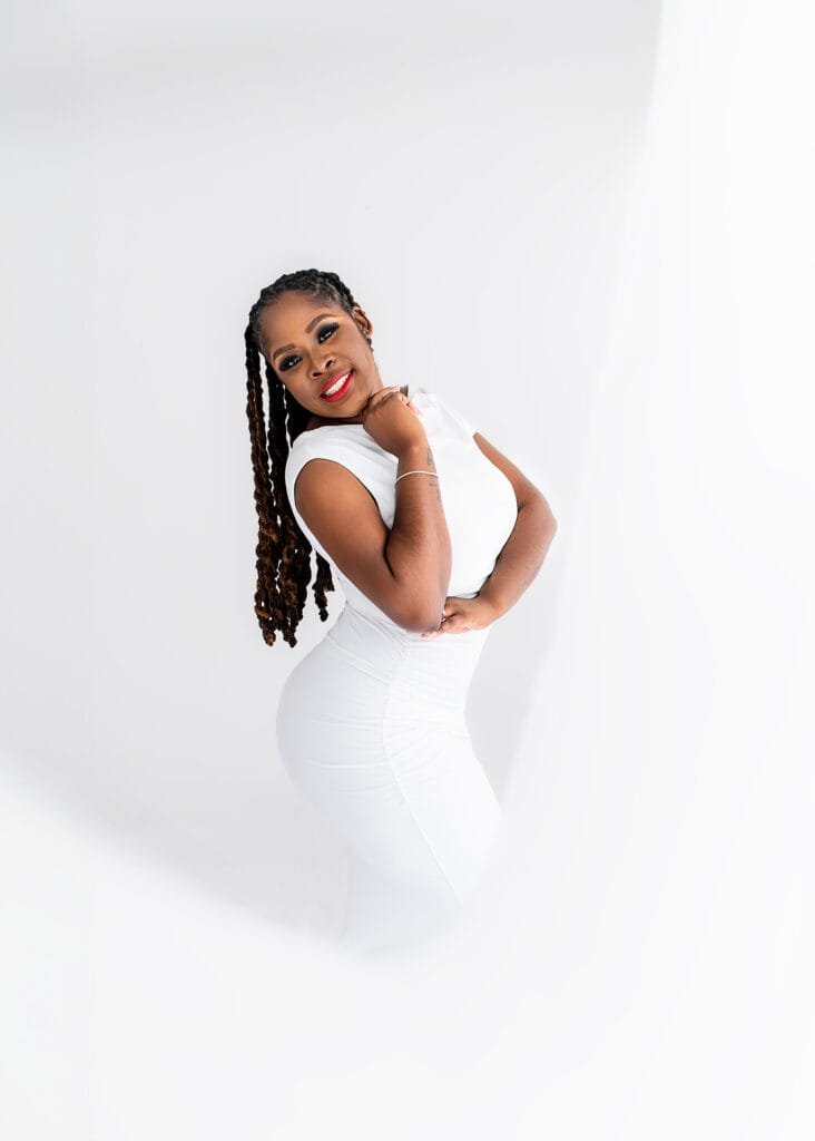 Glamorous birthday photography of a woman in a white dress, striking a confident pose in a studio setting.