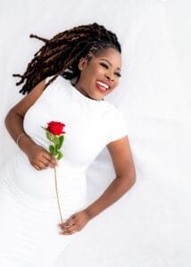 Studio birthday photography of a woman in a white dress, smiling while holding a red rose.