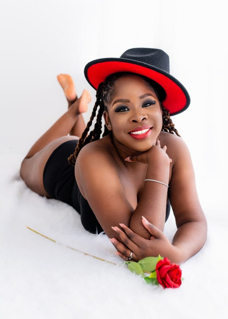 Elegant birthday photography featuring a woman in a stylish red and black hat, lying down with a red rose.
