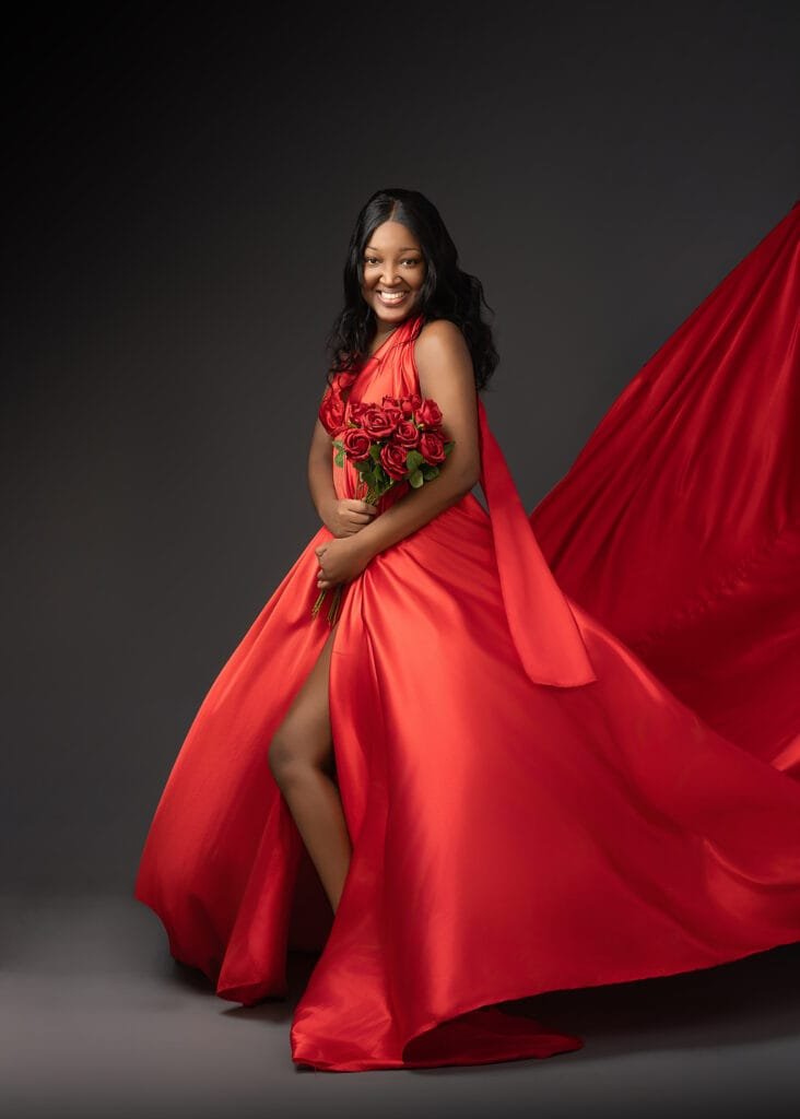 Birthday photography of a woman in a glamorous red dress, holding a bouquet of roses against a dark backdrop.