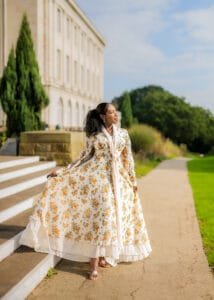 Outdoor birthday photography of a woman in a floral dress walking by a grand historic building.