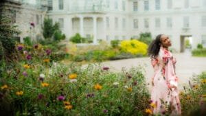 Outdoor birthday photography of a woman in a floral dress, smiling in a beautiful garden setting.