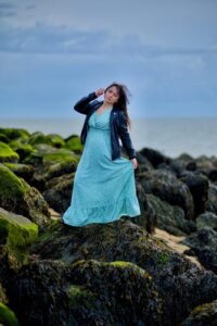 Fashionable Woman in Teal Dress and Leather Jacket by the Sea