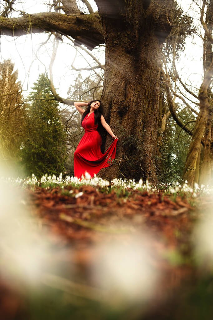 Smiling woman in a red dress amid blooming snowdrops next to a tree