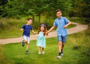 Three smiling children running and holding hands during a spring family photography session in Nottingham