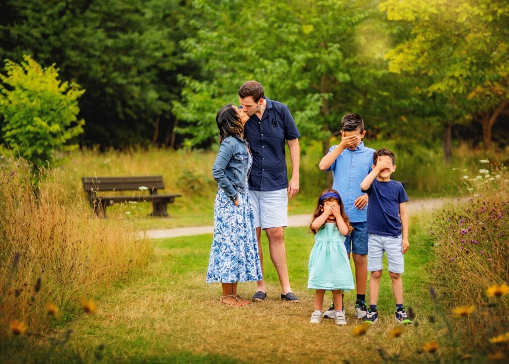 Parents kiss while children cover their eyes during a playful family photography session in Nottingham