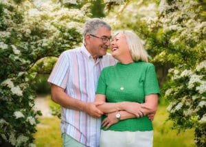 Senior couple laughing and hugging under blooming white trees during a family photography session in Nottingham