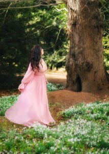 Woman in flowing pink gown admiring nature in a professional portrait.