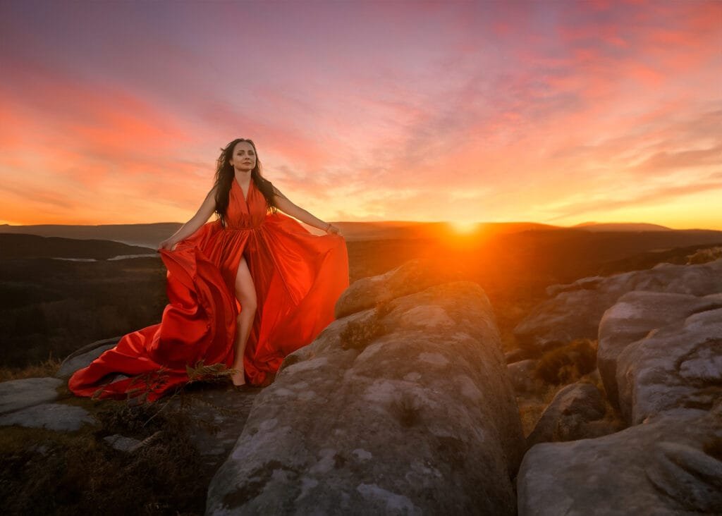 Female Portrait Photography – Confident woman in a flowing red dress poses at sunset on a rocky landscape, embracing empowerment and natural beauty in Nottingham.